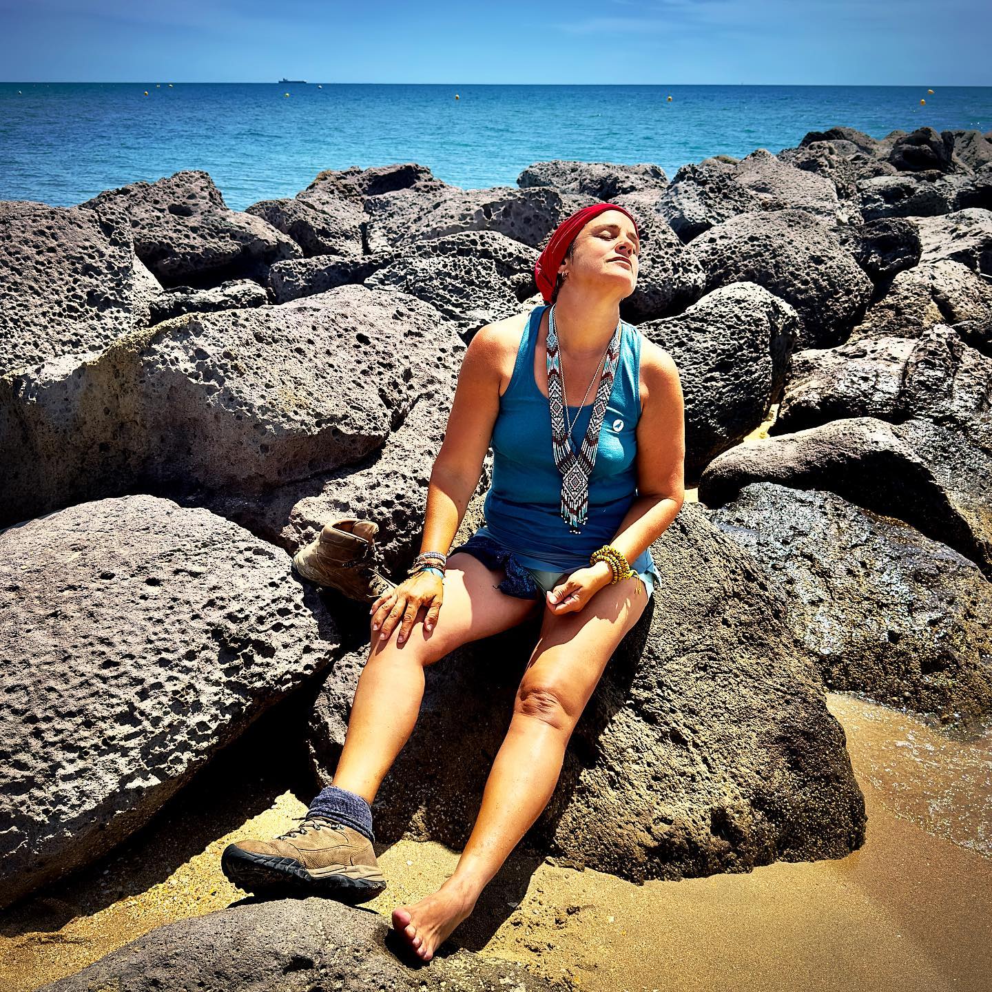 Céline assise sur une plage avec un fichu rouge sur la tête. blog Céline Anaya Gautier